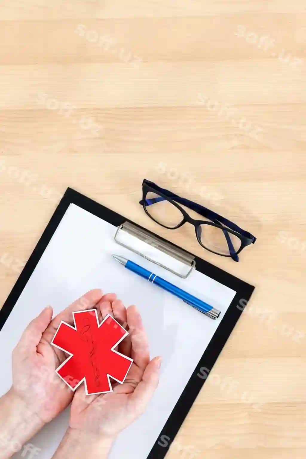 Ayollar qo'llari yong'i mezon yuqori ko'rinishda tibbiy belgi bilan papka va ko'z qo'lluklarini tutgan. | Female hands holding medical symbol clipboard glasses wooden desk top view